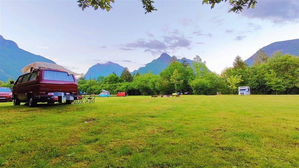 Peaceful campsite at Camp Vodenca surrounded by forest and mountains, with simple seating around a fire pit and camper vans in nature.