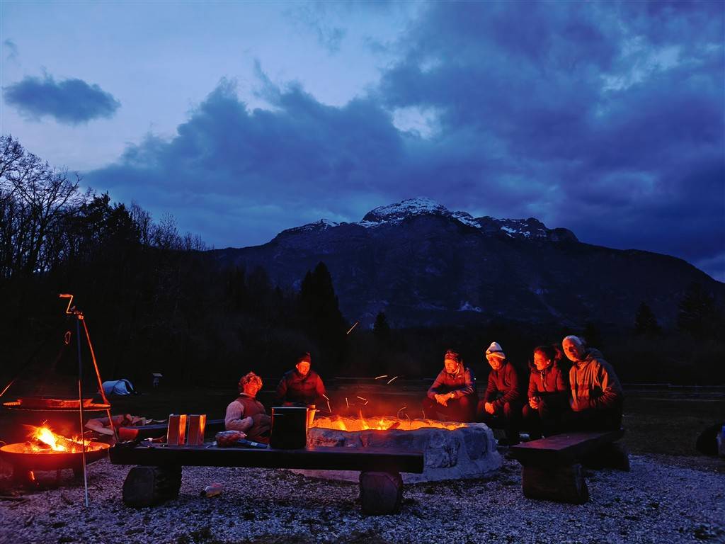 Campers sitting around a campfire at Camp Vodenca in Bovec with mountain views at dusk.