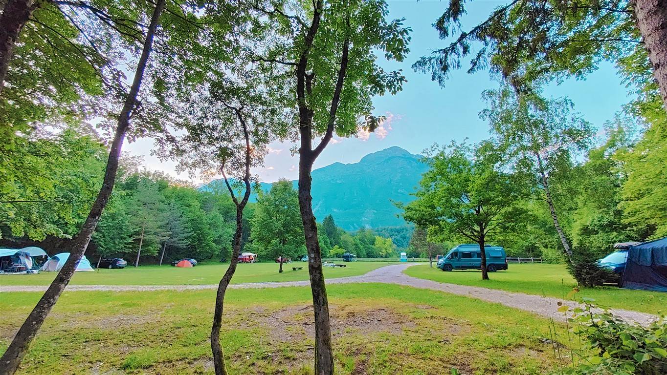 Camp Vodenca v Bovcu s šotori, kombijem, zelenim travnikom in pogledom na gore spomladi